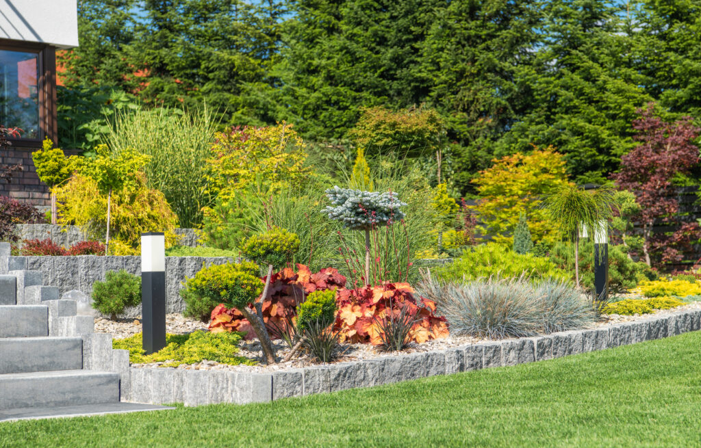 A beautifully landscaped garden with various plants, shrubs, and modern stone accents, featuring a well-maintained lawn and outdoor lighting.