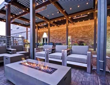 A stylish outdoor seating area under a SruXure pergola with string lights, featuring modern furniture and a rectangular fire pit.