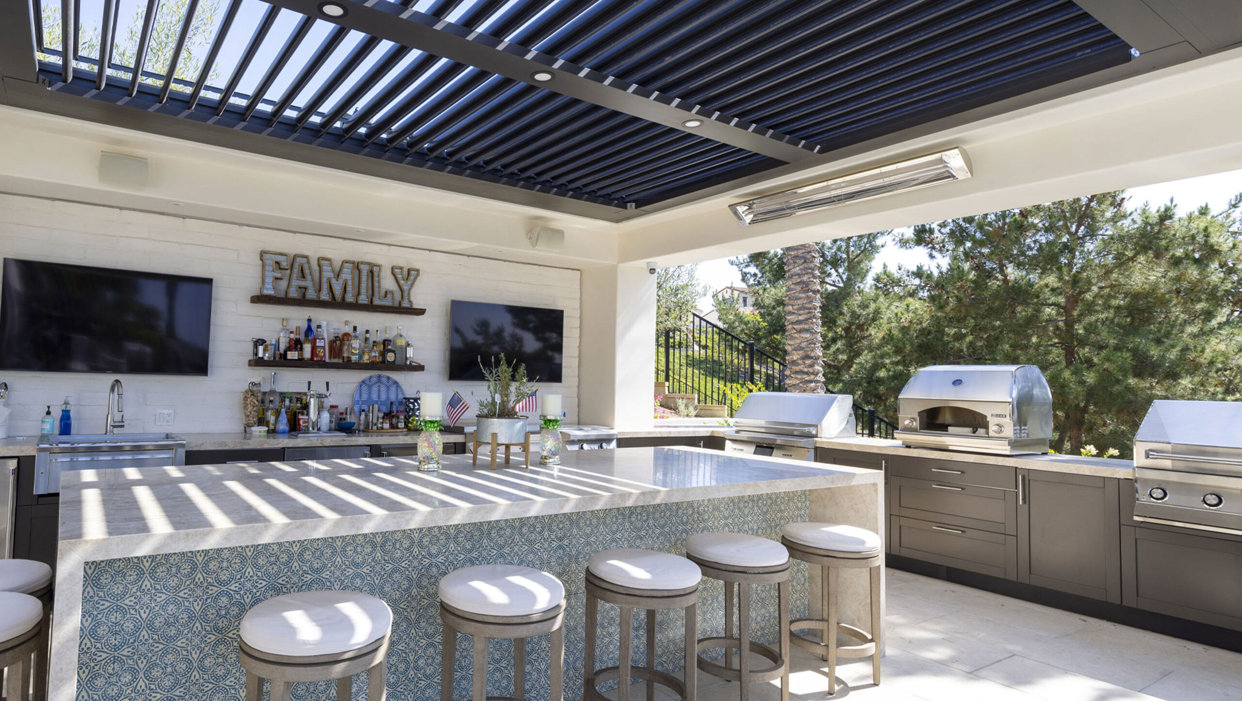 Modern outdoor kitchen with bar seating, TV, and grill under a pergola