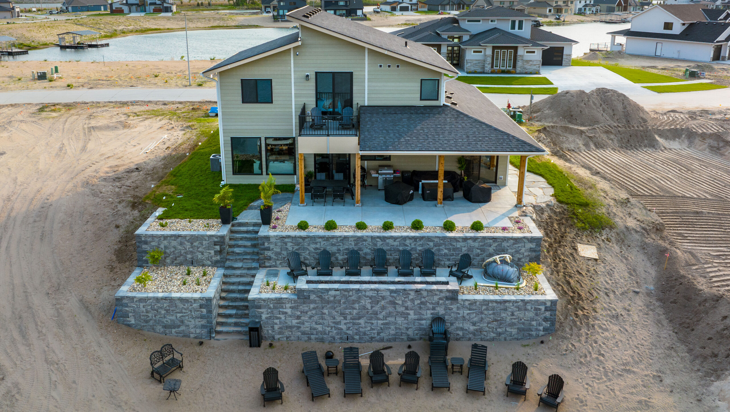 Aerial view of a lakeside house with a multi-level patio, retaining walls, and seating areas