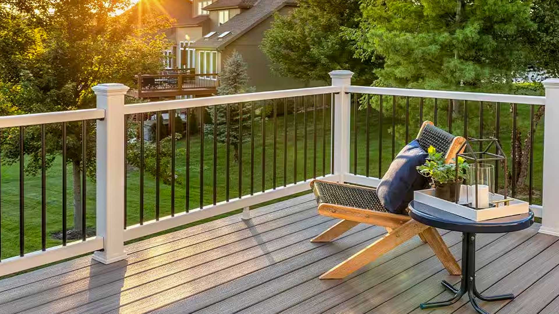 A cozy corner of a composite deck with a modern chair and small table, overlooking a green backyard at sunset.