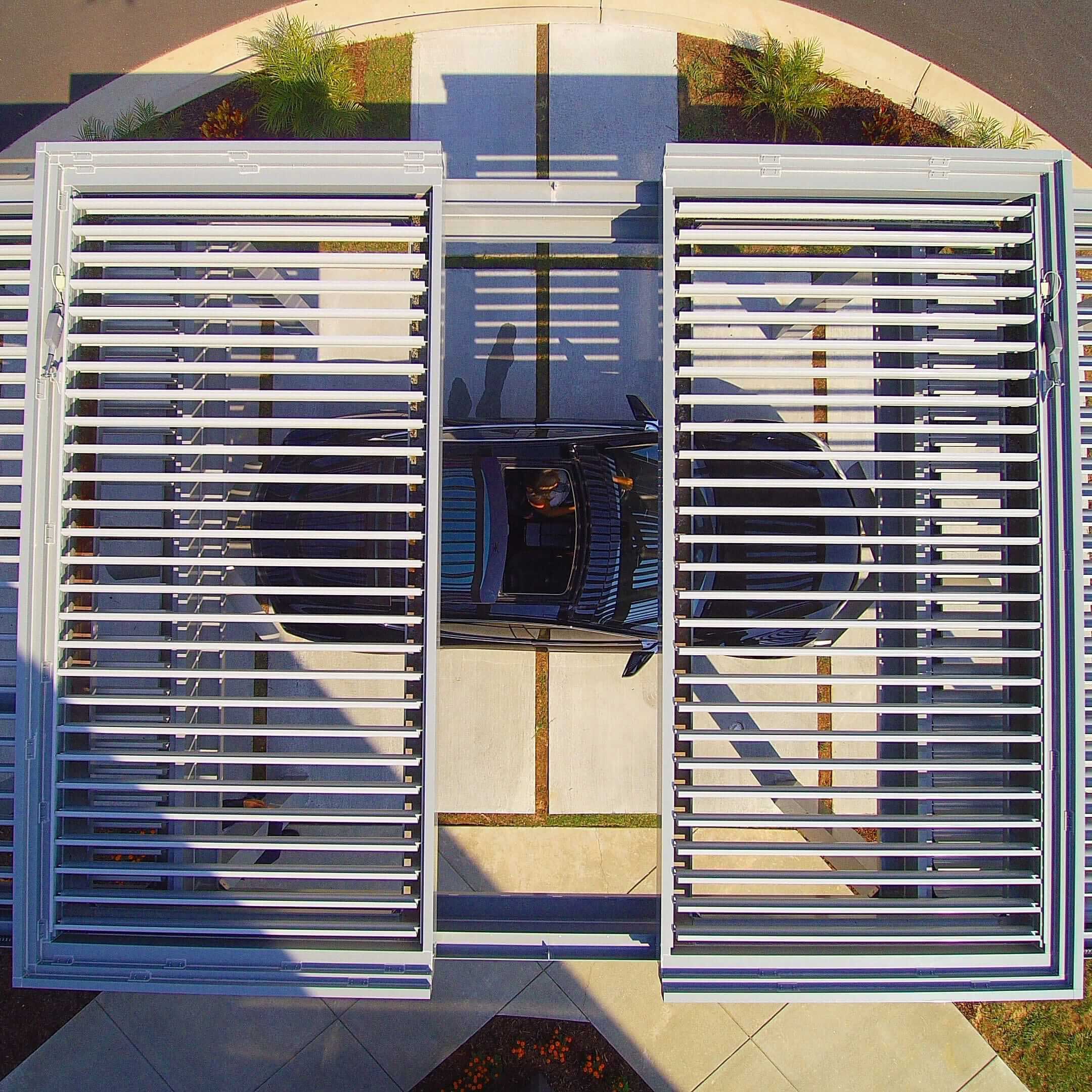 Aerial view of a SruXure pergola with adjustable louvers, installed over a driveway with a parked car beneath it.