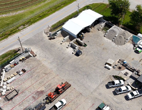Aerial view of Ground Builders Landscaping supply yard, featuring various materials and equipment, with vehicles and storage areas.