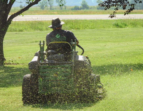 A Ground Builders Landscaping professional riding a lawn mower, cutting grass in a large open field.