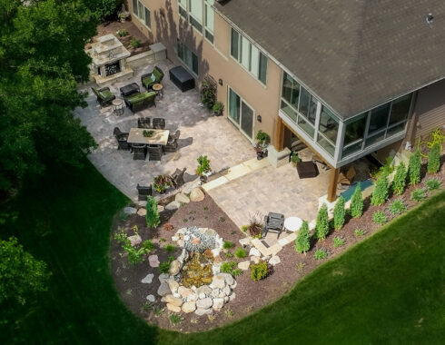 Aerial view of a beautifully landscaped backyard featuring a large patio with seating areas, an outdoor fireplace, and a decorative rock garden.