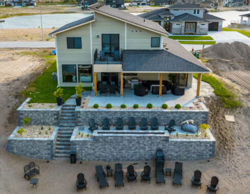 Aerial view of a lakeside house with a multi-level patio, retaining walls, and seating areas
